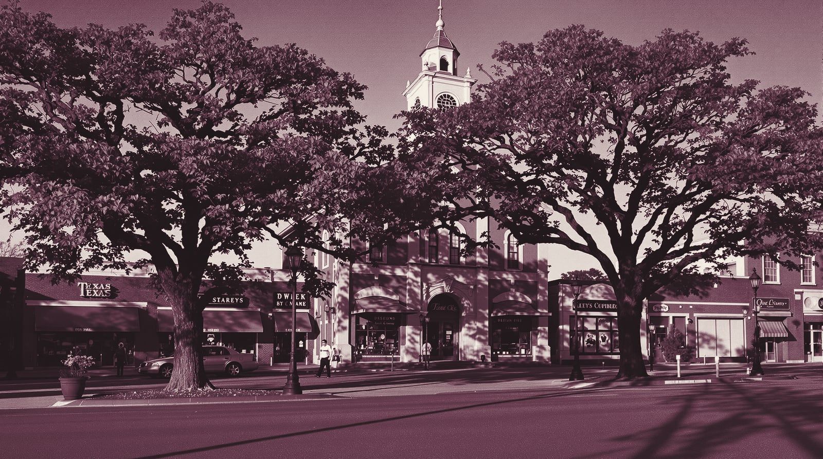 A small-town Texas courthouse square with a clock tower, live oaks and brick storefronts