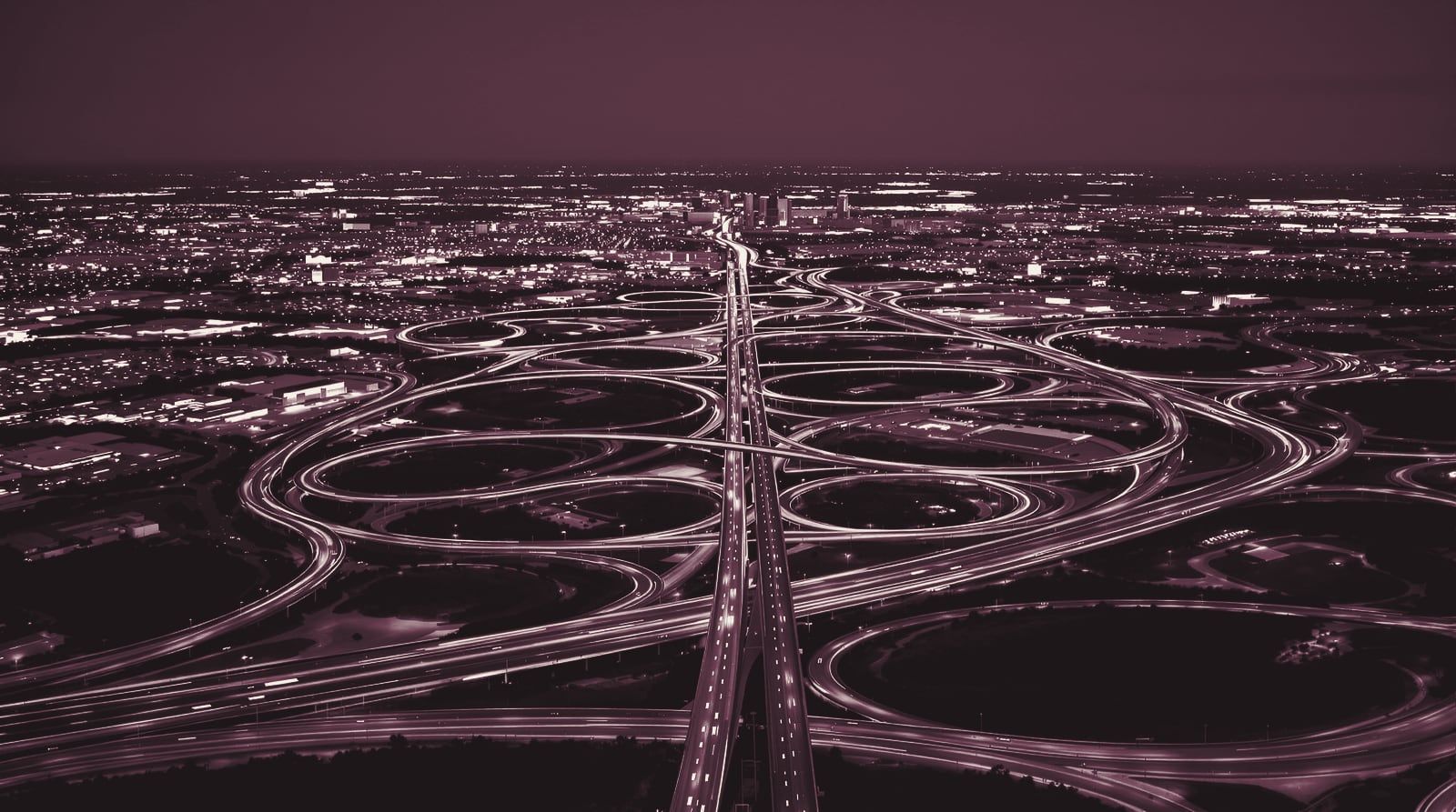 A multi-level freeway interchange at blue hour with light trails across a flat city