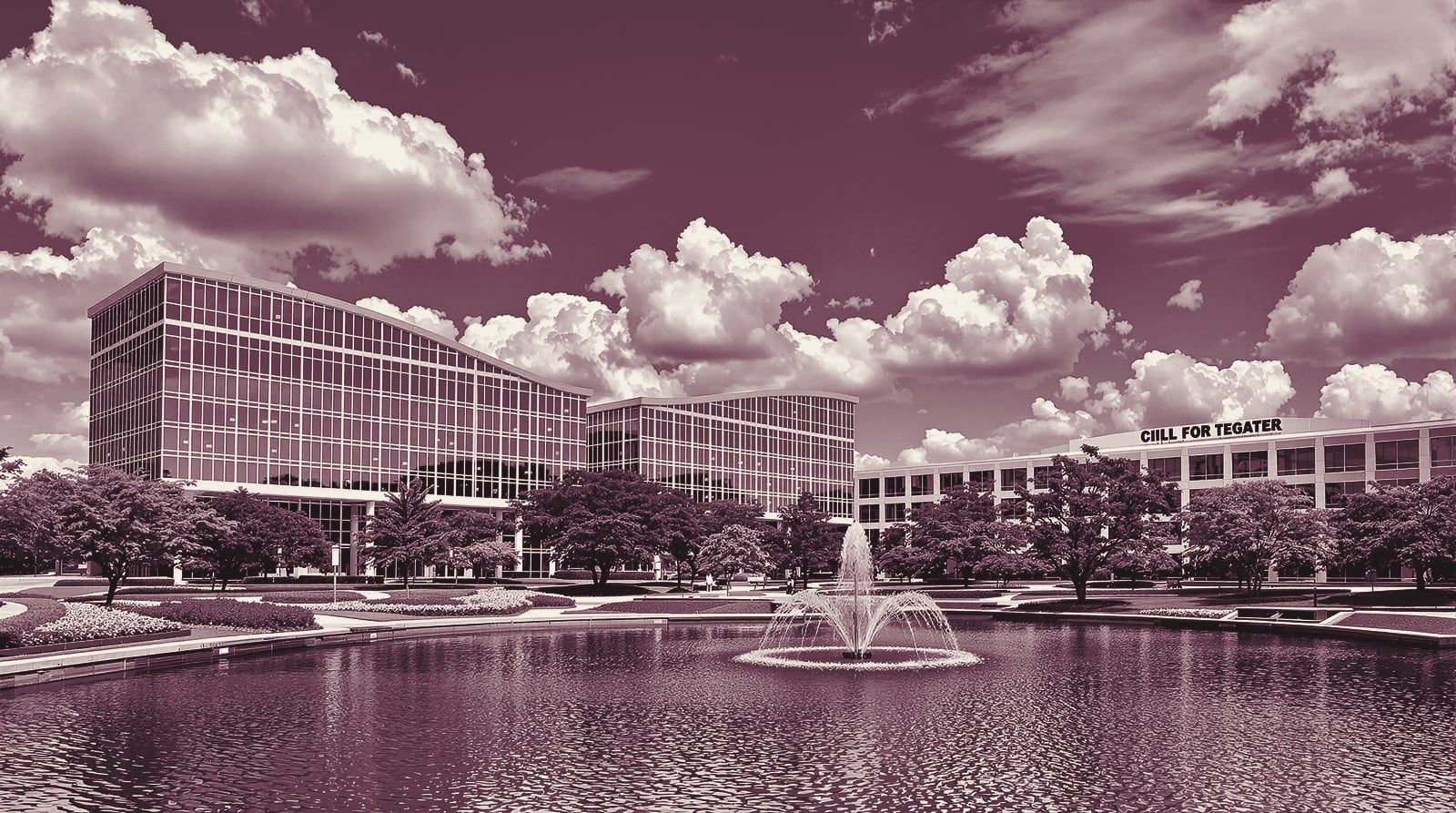 Glass office buildings around a pond with a fountain in a suburban office park