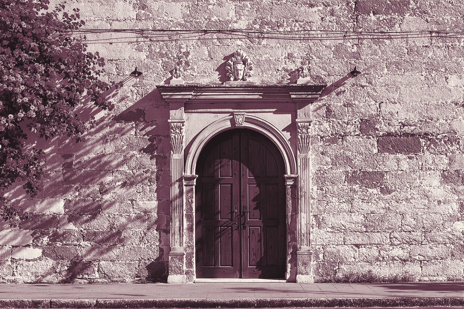An old limestone wall with a carved arched doorway and a heavy wooden door
