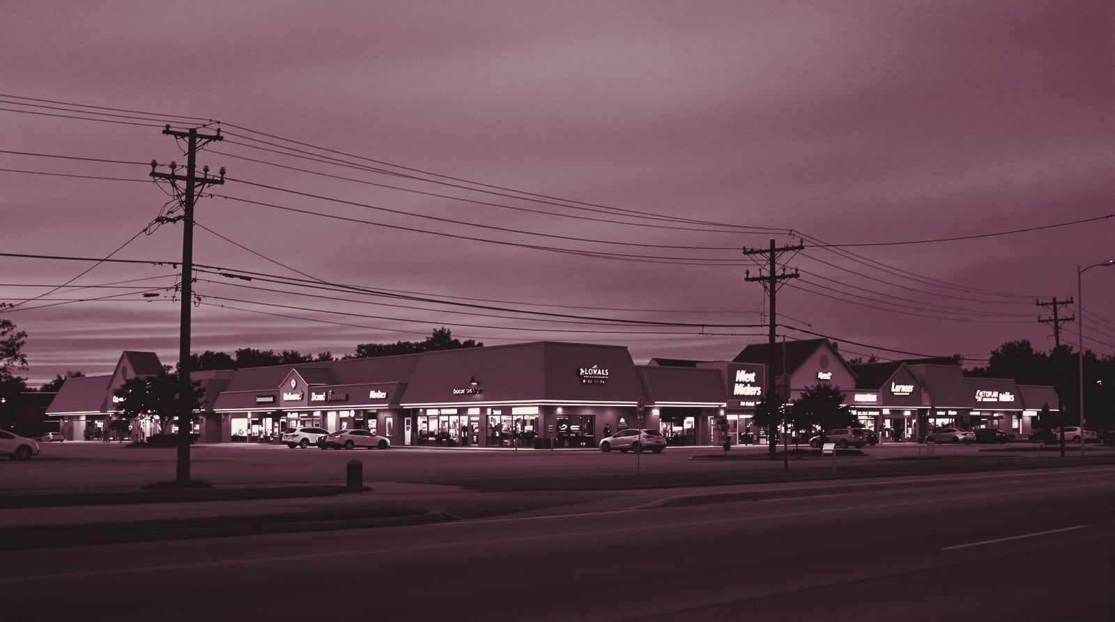 A suburban strip center at dusk beside a wide frontage road